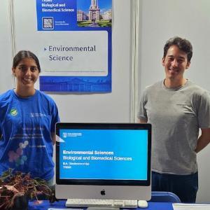 Student and Lecturer standing smiling at Environmental Science Stand at the Open day 2024. Desk set up with Computer demonstration.